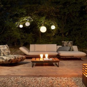 Nächtliche Szene auf einer Holzterrasse mit leuchtenden Kugellampen, die in den Bäumen hängen, und darunter steht eine Lounge dekoriert mit Kissen auf einem Holzplateau