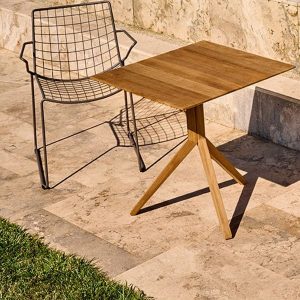 Ein quadratischer Holztisch auf einem schlanken dreifußigem Gestell und einem Stuhl aus Aluminiumgeflecht daneben