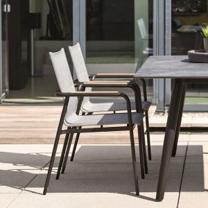 Ein Tisch mit einer grauen Tischplatte und grauen Füßen mit zwei Stühlen mit Teakarmlehnen